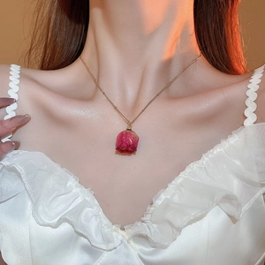 Detailed close-up of a gold necklace with a real dried red rose flower pendant on a model