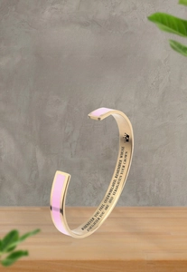 Macro detail of gold stainless steel bangle with pink enamel and engraved crown daughter quote