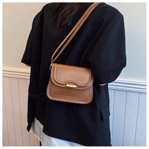 Détail d'un sac besace marron avec fermoir tournant en métal doré et blazer noir élégant