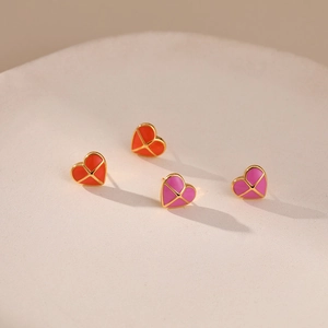 Detail of heart-shaped gold earrings with red and pink enamel on a stone pedestal