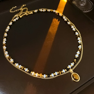 Detail of double-layer gold necklace with beaded chain and oval tiger eye stone pendant