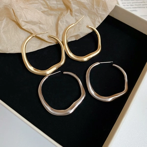 Close-up of irregular twisted gold and silver hoop earrings on a black velvet box