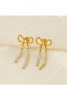 Detail of golden bow earrings with sparkling white zircon tassels in titanium steel