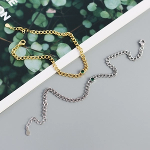 Detailed view of gold and silver tank chain bracelets featuring green round gemstone inlays