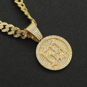 Gold-plated Cuban chain necklace with iced-out round pendant on dark background
