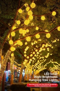 Dettaglio di luci solari a sfera in rattan a LED giallo caldo appese agli alberi