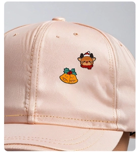 Detail of Christmas reindeer and bells enamel pins attached to a pink satin baseball cap