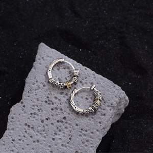 Retro Tibetan style hoop earrings with golden prayer wheel on volcanic stone background