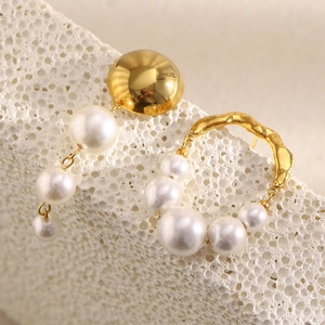 Detail of 18K gold plated stainless steel pearl earrings on white stone background