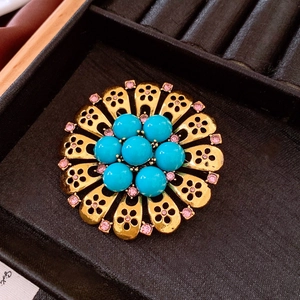 Macro detail of vintage floral brooch with turquoise stones and pink crystals on black velvet