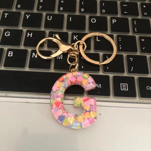 Detail of letter G resin keychain with colorful heart sequins on a laptop keyboard