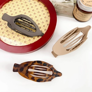 Three large matte oval hair claws in grey, beige, and tortoiseshell on a white surface