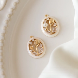 Macro view of gold-plated tulip charms with cream enamel and pearl accents on white silk