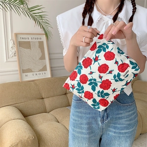 Floral makeup bag with red roses and green leaves held by a model in a cozy interior