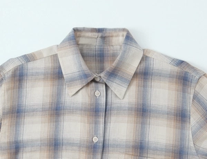 Dettaglio del colletto di una camicia a quadri con bottoni beige e tessuto blu e crema