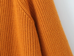Gros plan d'un pull en tricot orange montrant la texture des mailles et les coutures