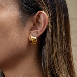 Macro view of gold stainless steel C-hoop earring worn by a model in a minimalist style