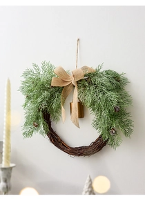 Close-up of Christmas wreath with pine needles, burlap bow and bell on a white wall
