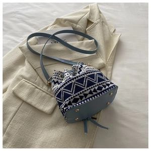 Detail of geometric blue fabric bucket bag with drawstring on a beige blazer background