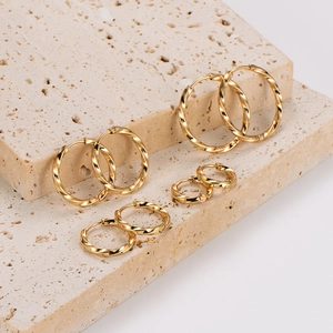 Set of four sizes of gold-plated twisted hoop earrings on a textured stone display