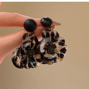 Hand holding floral leopard print resin C-shaped drop earrings with gold rose center