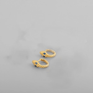 Detailed macro shot of golden snake-shaped earrings featuring sparkling blue gemstone eyes