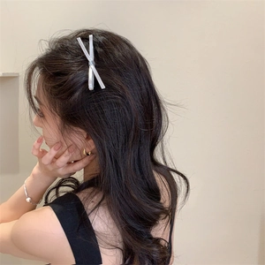 Detail view of a silver crisscross hair clip worn on a model's hair in an elegant style
