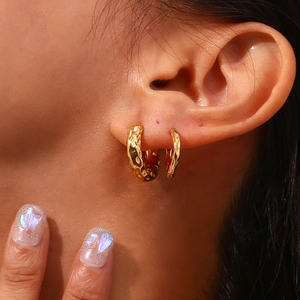 Close-up of golden irregular moon-surface earrings worn in multiple ear piercings