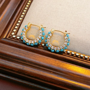 Close-up of vintage C-shape gold earrings inlaid with turquoise and white zircon stones