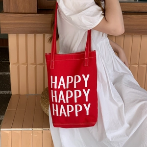 Minimalist red canvas tote bag with white Happy print shown on a female model shoulder