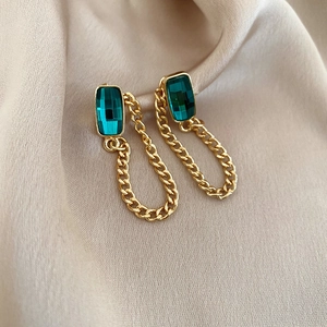 Detail of vintage gold earrings with emerald green crystals and chunky Cuban chain links
