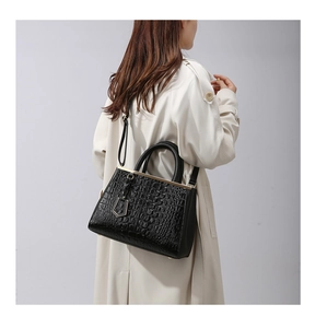 Dettaglio della borsa nera a motivo coccodrillo indossata con un trench beige