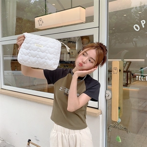 White quilted makeup bag with heart pattern held by a model in front of a cafe