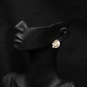 Detailed view of spiral golden earrings with three white pearls on a dark studio background