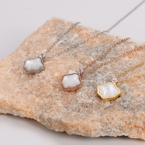 Three minimalist fan-shaped shell necklaces in silver, gold, and rose gold on stone