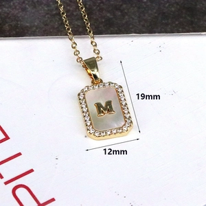 Macro shot of 18K gold letter M necklace pendant with mother of pearl and zircon stones