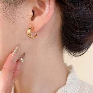 Detailed side view of minimalist C-shaped gold stud earrings on model with metallic luster