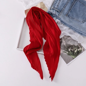 Flat lay of pleated red silk scarf styled with jeans and a floral book on white background