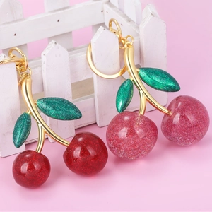 Detail view of red and pink glitter cherry keychains leaning on a white fence prop