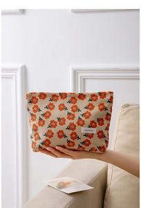 Close-up of vintage orange floral corduroy makeup bag held by hand in a warm home setting