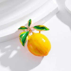 Cute yellow lemon brooch with green leaves and gold finish on a white background