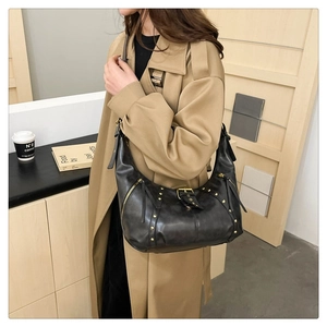 Detail of a black hobo bag with gold rivets and wide strap on a khaki trench coat