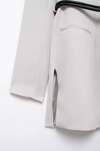 Detail of light gray blazer fabric showing texture, side slit, and black waist belt