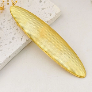 Detailed view of golden oval alloy hair clip with textured ridges on stone surface