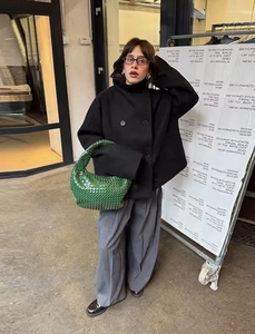 Close-up of black double-breasted woolen jacket with grey wide-leg trousers and green bag