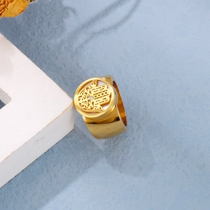 Detail of gold wide band ring featuring Hamsa Hand cutout and a small clear crystal