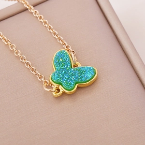 Golden chain necklace featuring a green butterfly pendant on a beige jewelry box edge