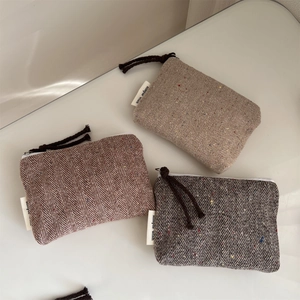 Close-up of three herringbone tweed mini pouches with colorful dots and top zippers