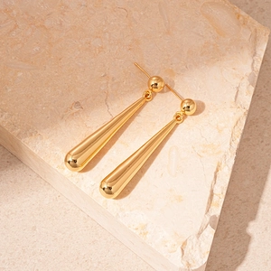 Macro shot of minimalist gold teardrop earrings on a textured stone base with soft shadows