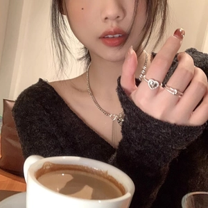 Silver heart necklace and stacked rings set worn by a model in a cozy cafe setting